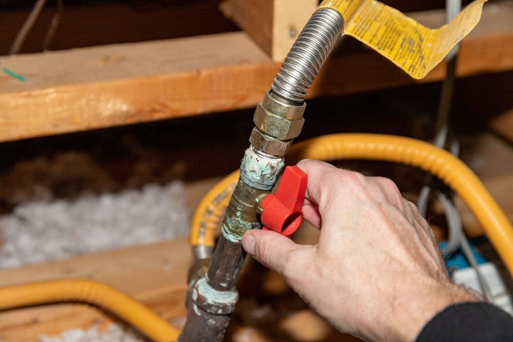 Hand turning a red gas shut-off valve on a flexible gas line