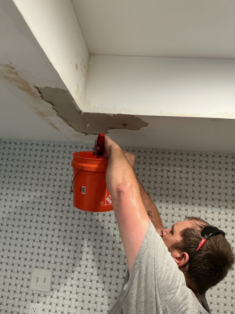 Person catching a ceiling leak with an orange bucket