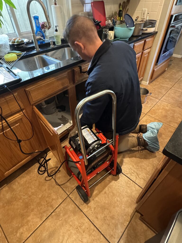 PlumbingPro technician clearing a kitchen drain with a drain machine
