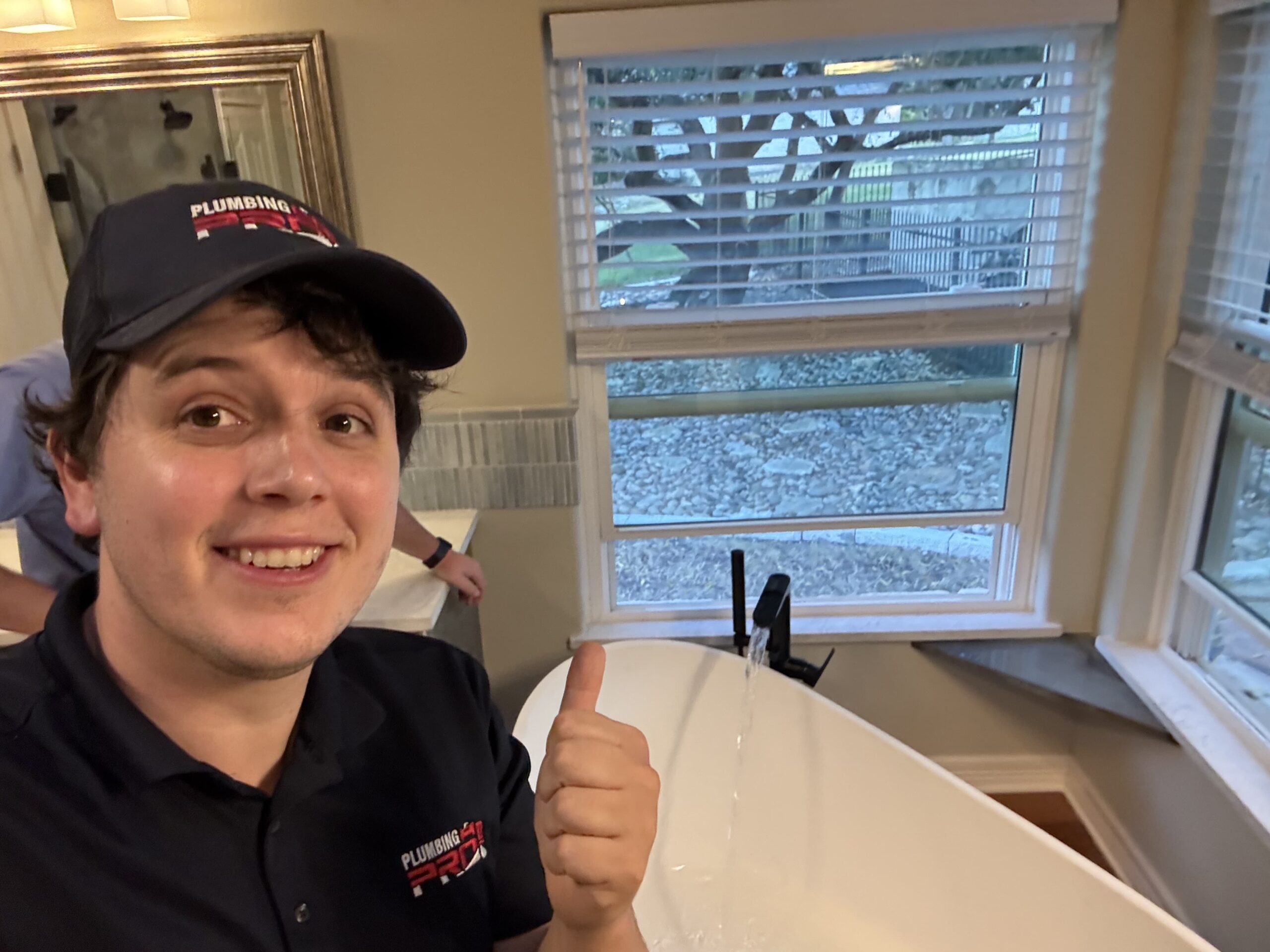 Smiling PlumbingPro technician giving a thumbs up beside a new bathtub