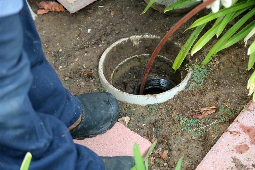 Plumber kneeling beside an outdoor sewer cleanout
