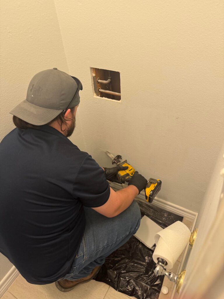 PlumbingPro plumber working on a fixture in a bathroom wall