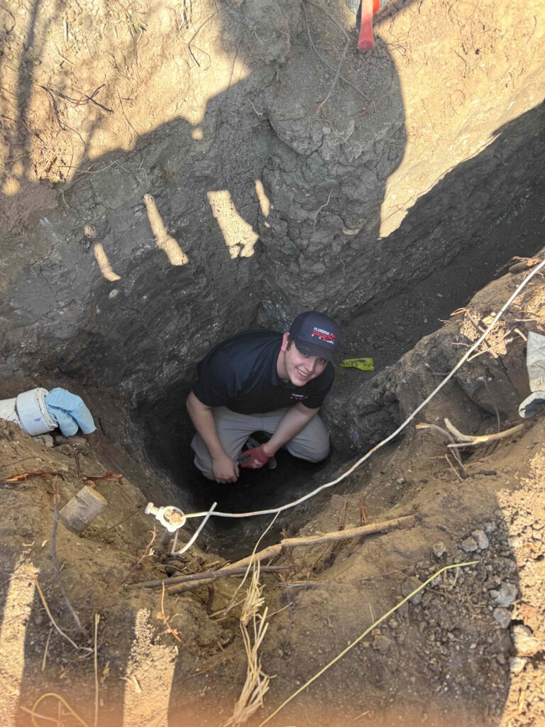 PlumbingPro technician working in a deep excavated trench