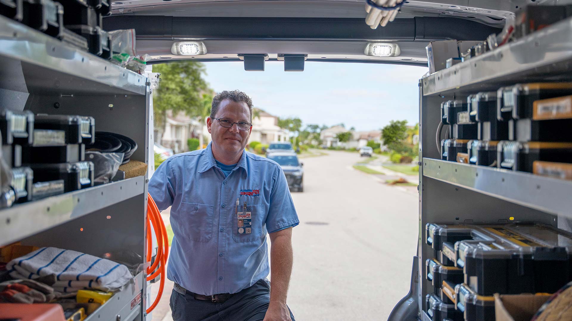 PlumbingPro plumber standing at the open rear doors of a service van stocked with parts and tool cases