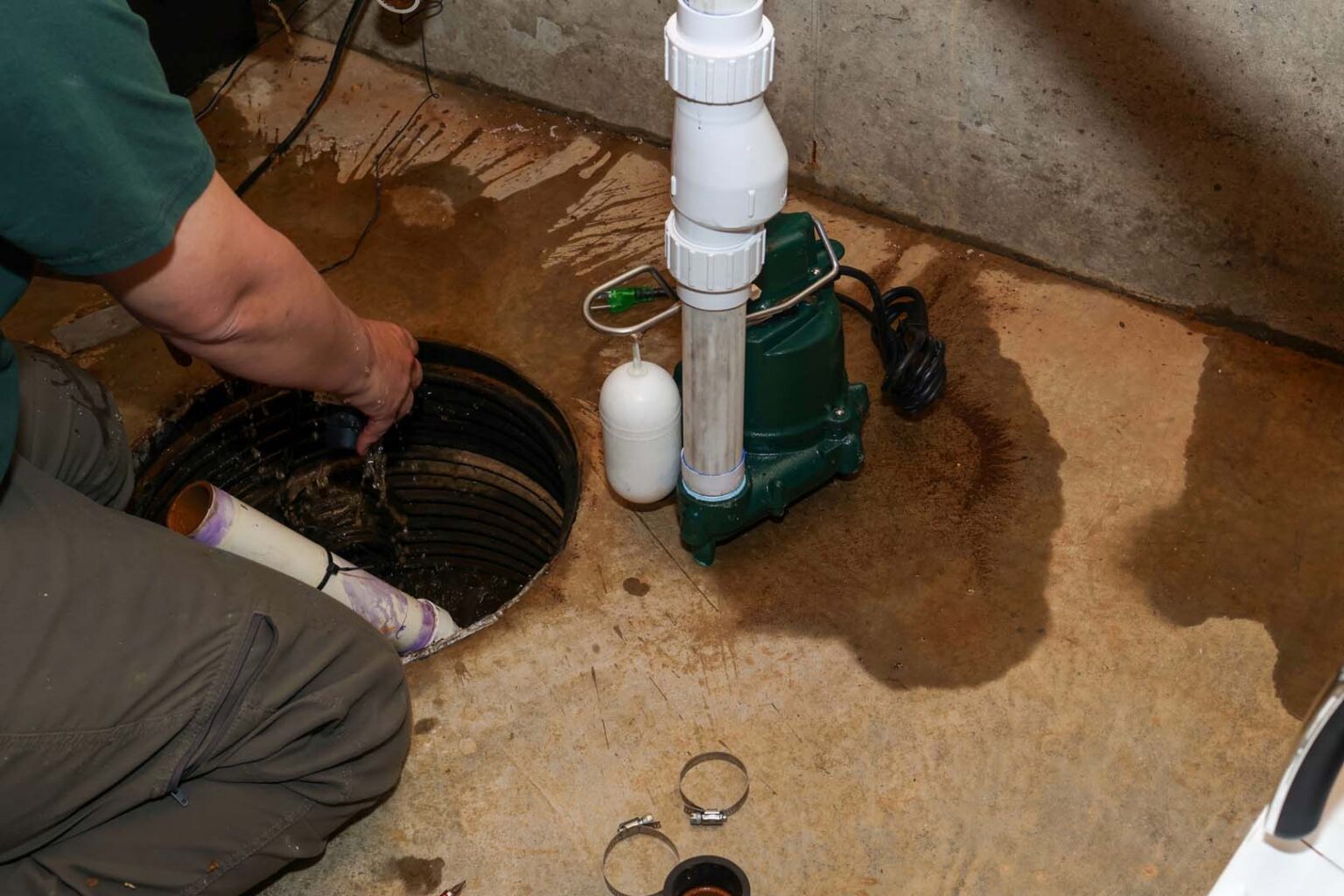 Plumber installing a new sump pump and discharge pipe at a basement sump pit