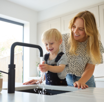 Mother and young son filling a glass at a kitchen faucet