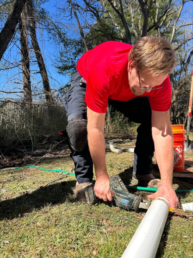 Technician in a red shirt cutting a white PVC pipe outdoors