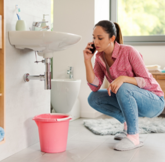 Woman on the phone looking at a leak under a bathroom sink