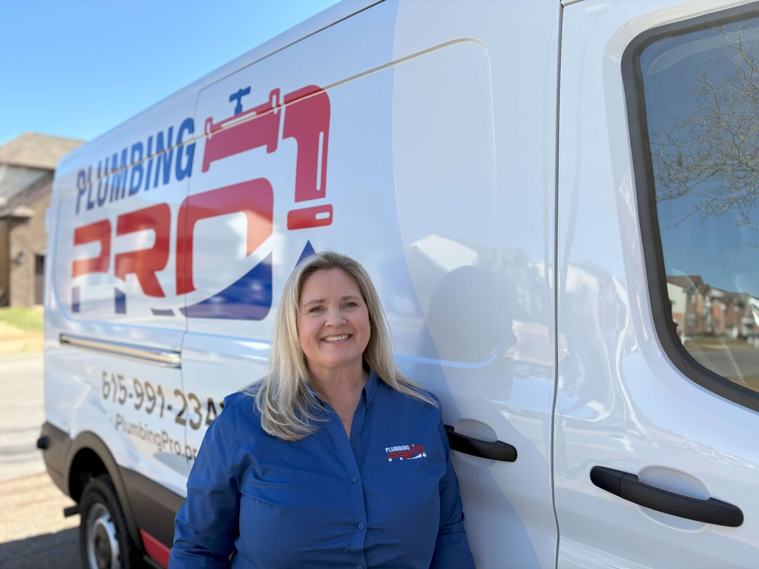 Smiling woman in a PlumbingPro shirt standing beside a PlumbingPro van