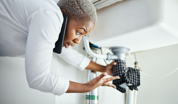Woman on the phone checking a leak under a sink