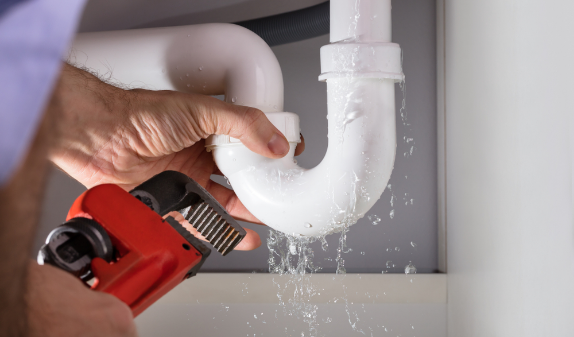 Plumber repairing a leaking P-trap with a red wrench