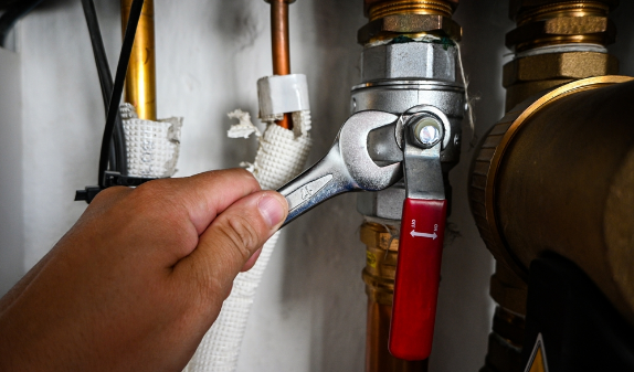 Hands tightening a pipe fitting with a wrench next to a red valve