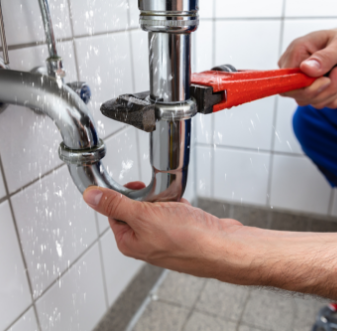 Plumber loosening a sink drain pipe with a red wrench