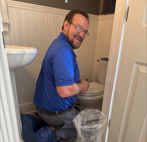 Technician in a blue uniform repairing a toilet