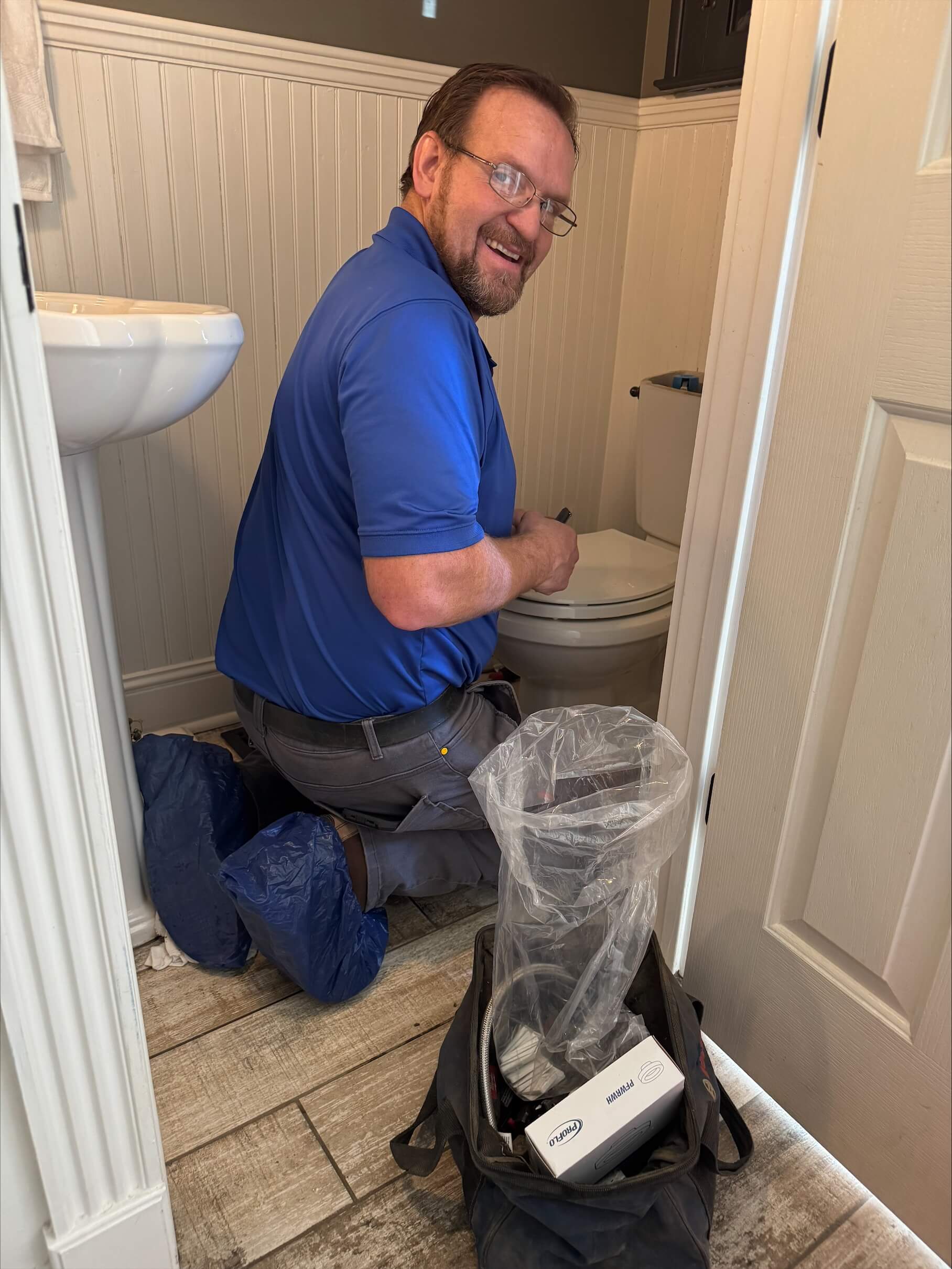 Technician in a blue uniform repairing a toilet