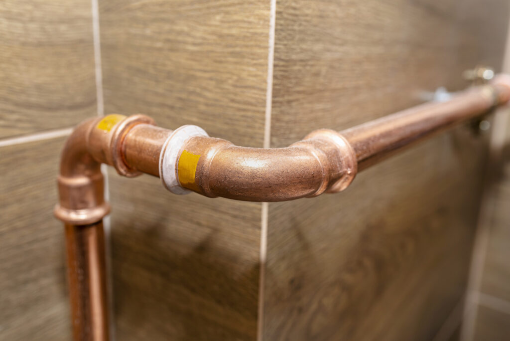 Copper pipe with soldered fittings on a tiled wall