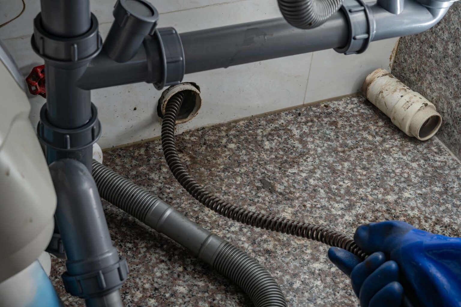 Gloved hand feeding a drain snake into a sink drain line