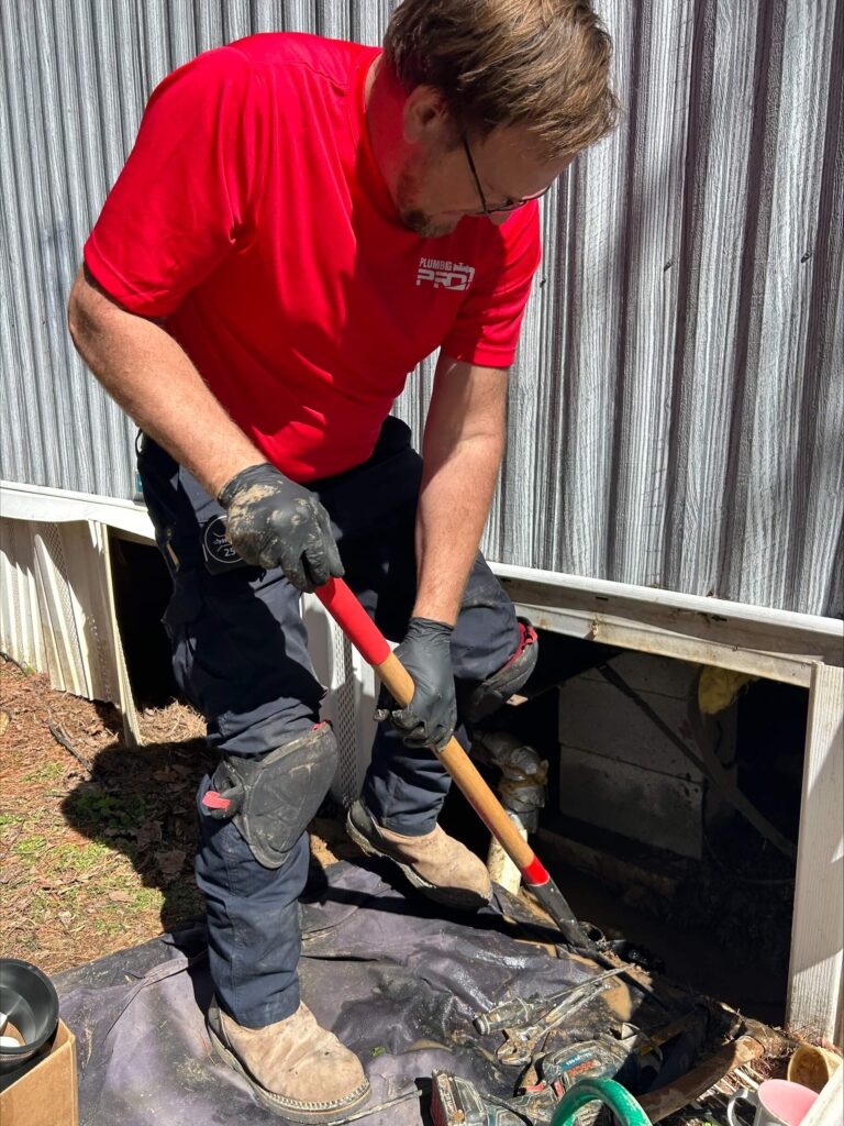 Technician in a red shirt digging in a yard to reach a pipe