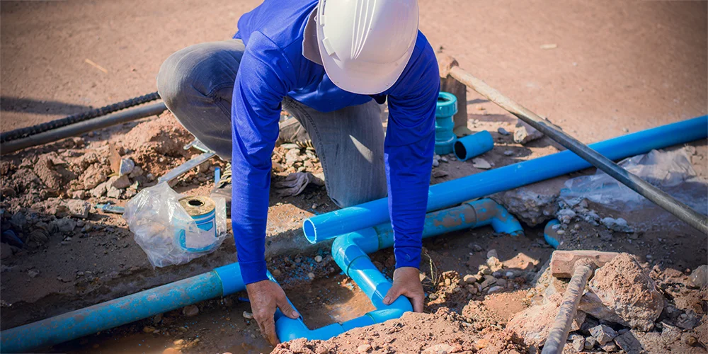 Worker repairing blue water pipes in an excavation