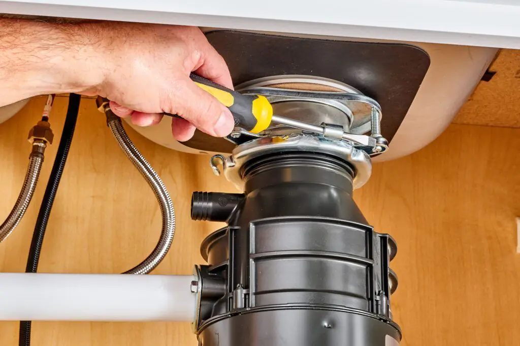 Hands repairing a garbage disposal with a screwdriver