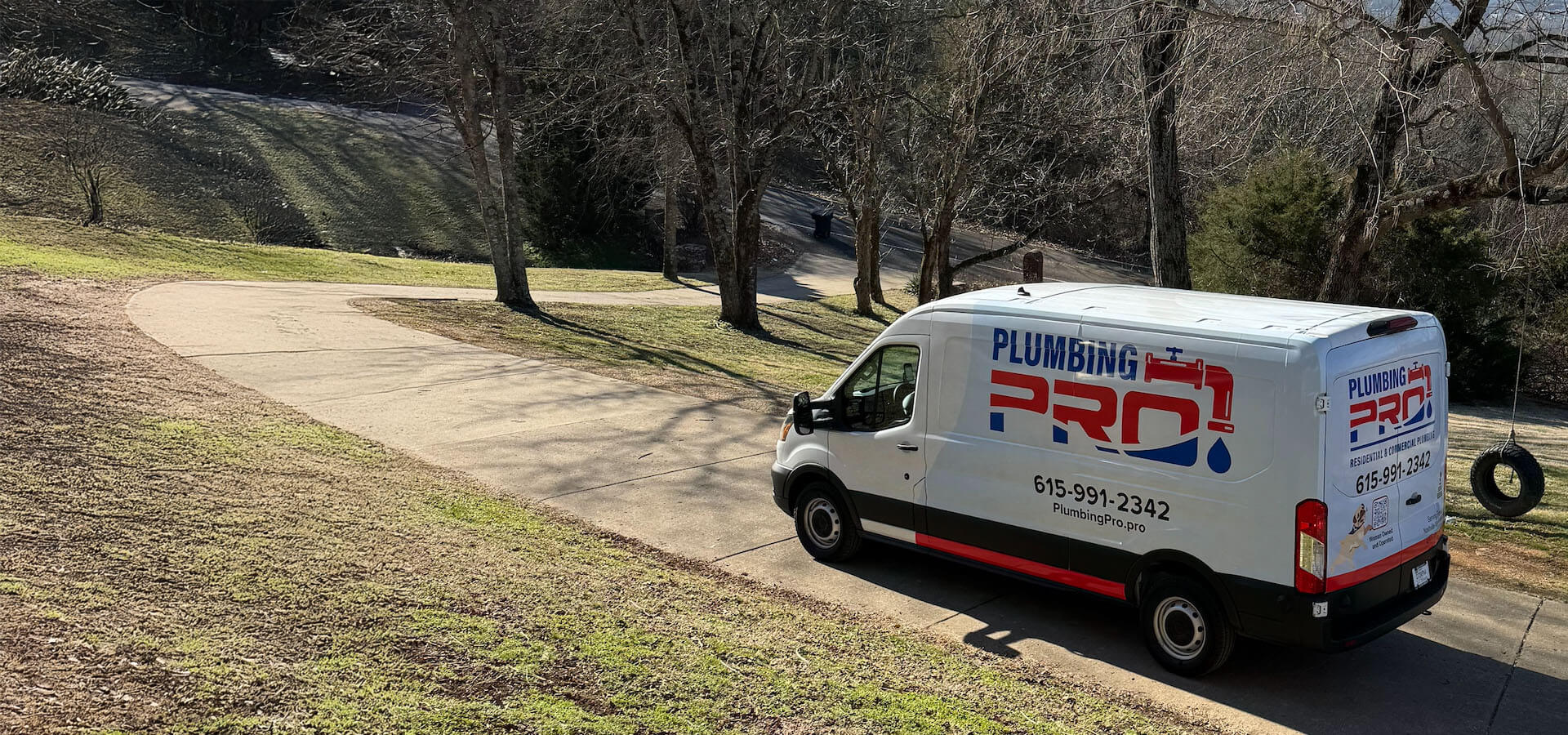 PlumbingPro service van parked beside a tree-lined lawn