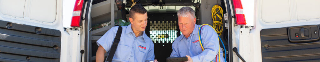 Two PlumbingPro technicians looking at a tablet inside a service van