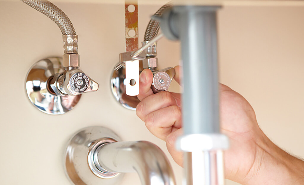 Hand connecting chrome supply valves under a bathroom sink