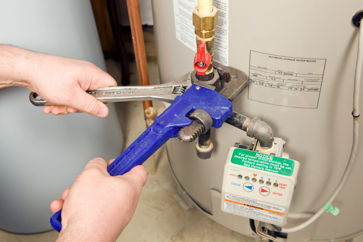 Hands tightening a water heater valve with a blue pipe wrench