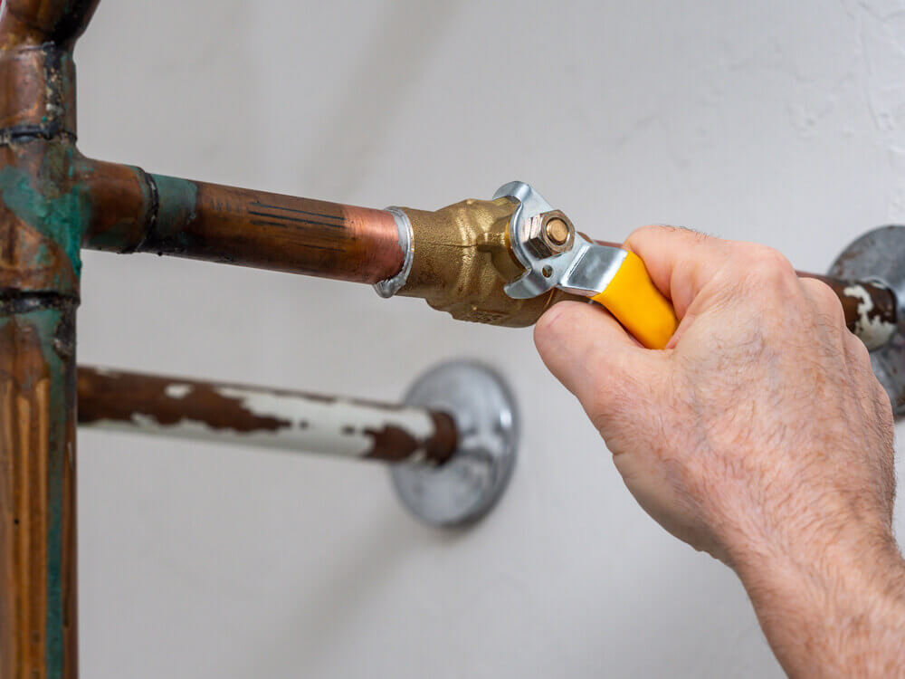 Hand turning a shut-off valve on a copper pipe with a wrench
