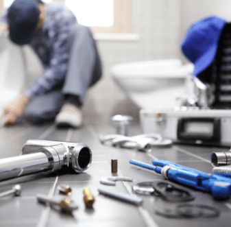Plumber working on a toilet with tools laid out on the floor