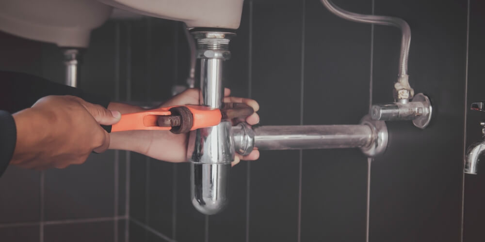 Plumber tightening a chrome sink drain pipe with a red wrench