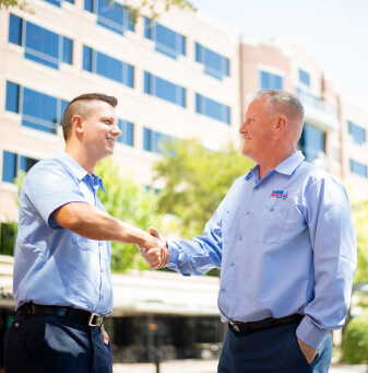 Two technicians in blue uniforms shaking hands outside an office building