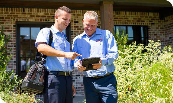 Two PlumbingPro technicians reviewing a tablet outside a home