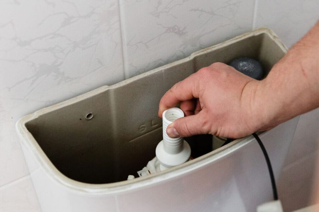 Hand adjusting the fill valve inside a toilet tank