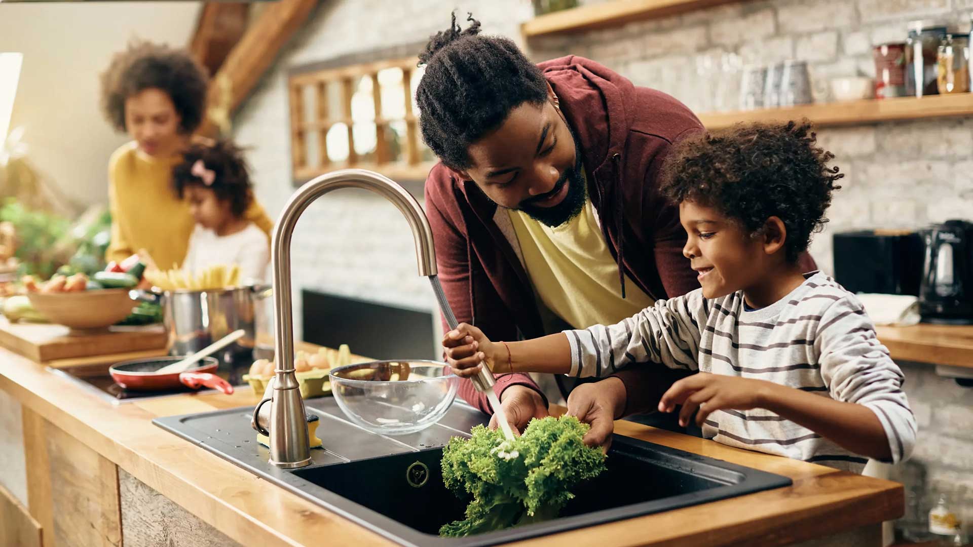 Family washing vegetables together at a kitchen sink