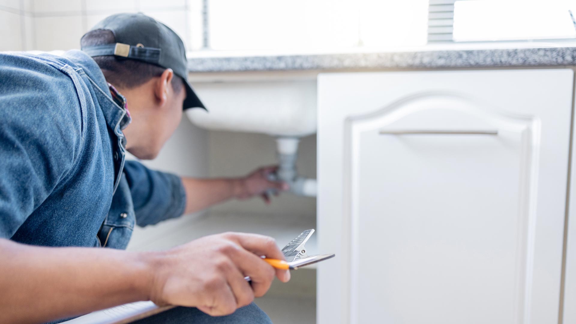 Plumber inspecting the plumbing under a kitchen sink