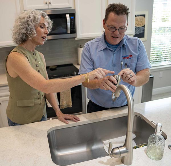 PlumbingPro plumber talking with a homeowner at a kitchen sink