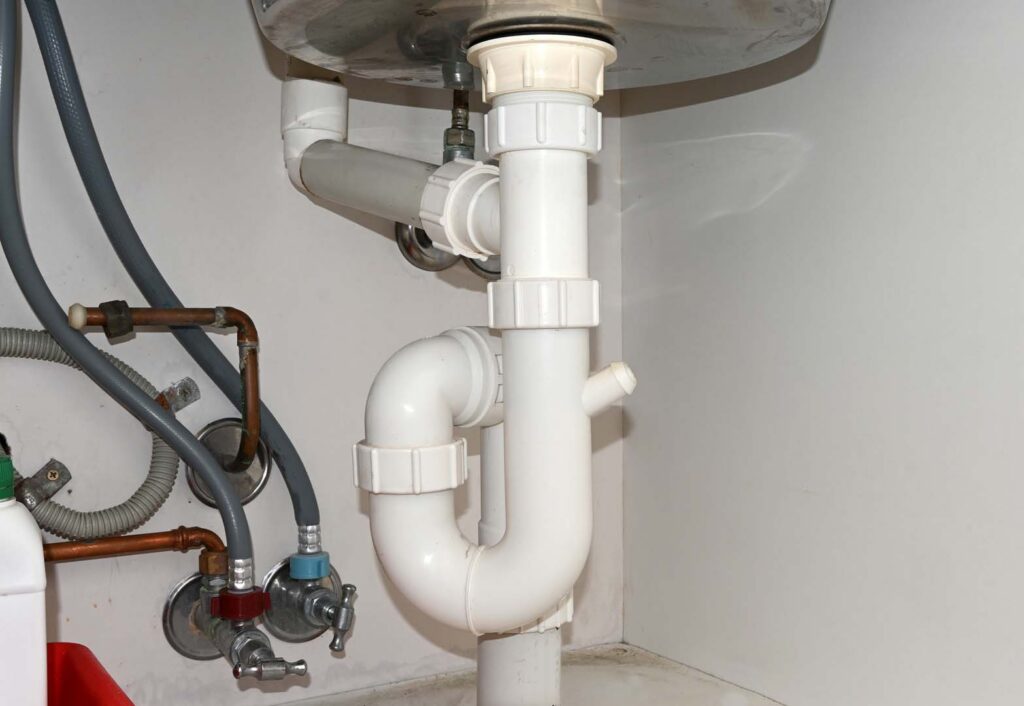 White PVC P-trap and water supply valves under a sink
