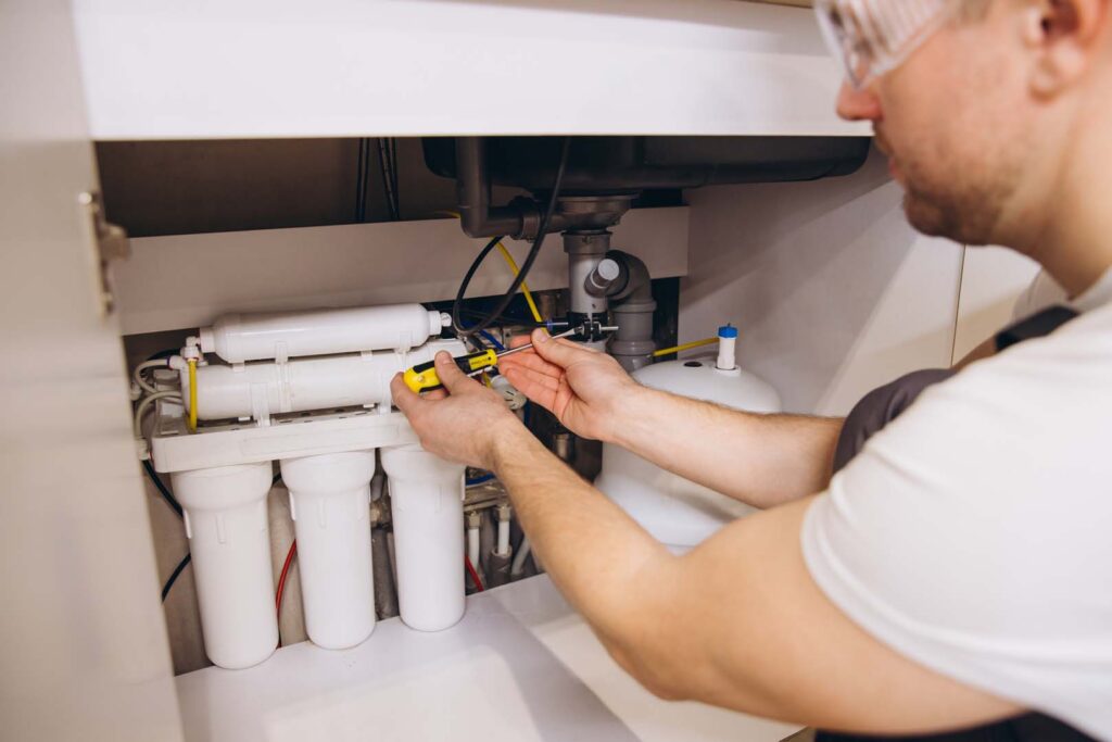 Plumber servicing a reverse osmosis water filter system under a kitchen sink