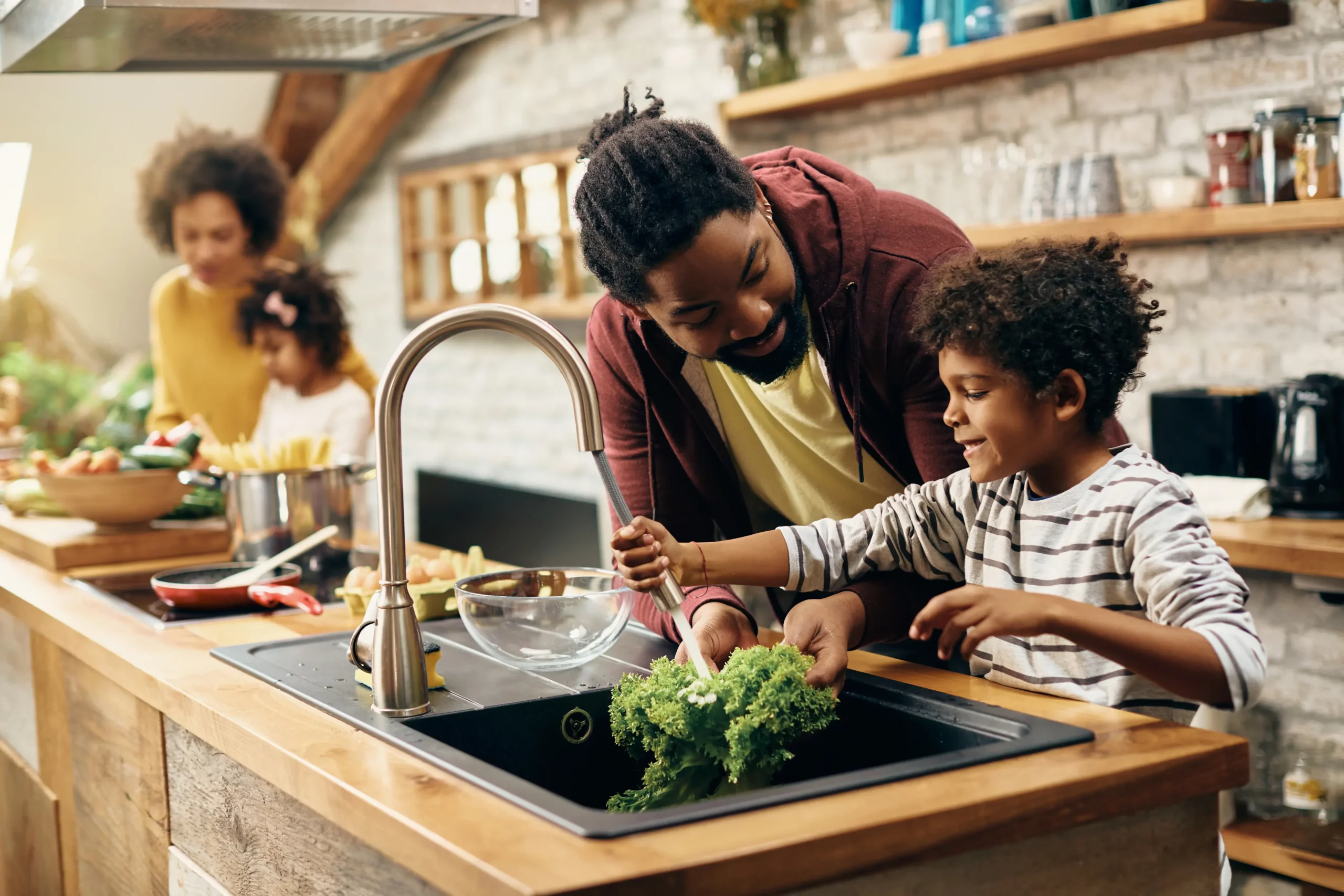 Family washing vegetables together at a kitchen sink
