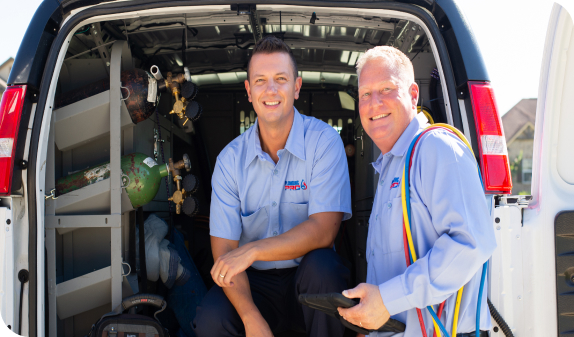 Two smiling technicians sitting in the open back of a service van