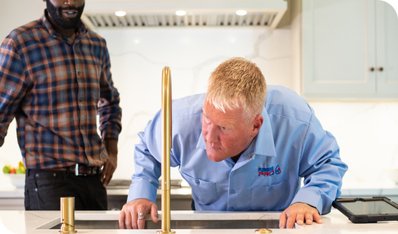 Plumber inspecting a kitchen faucet as a homeowner looks on