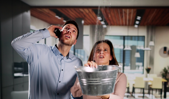 Worried couple catching a ceiling leak in a metal bucket