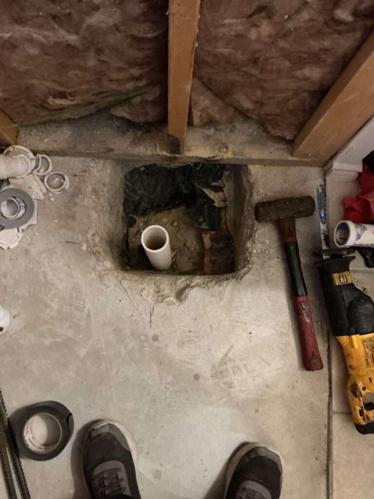 Completed 2-inch drain pipe in a concrete floor opening with tools nearby