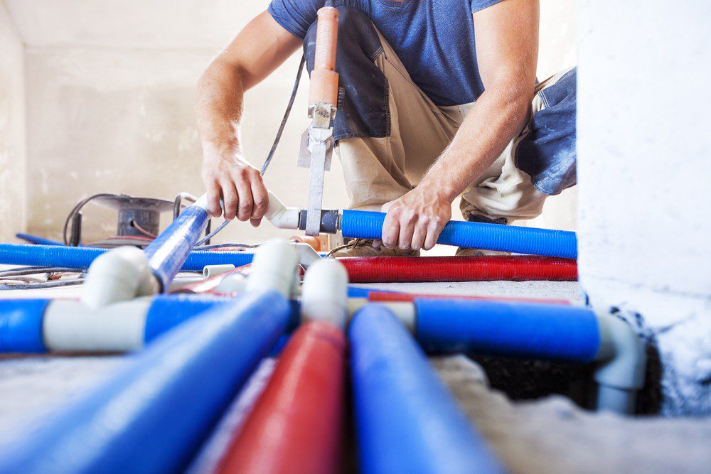 Plumber connecting blue and red plastic water pipes on a job site