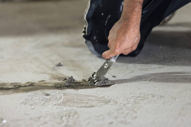 Worker patching a crack in a concrete slab floor with a trowel