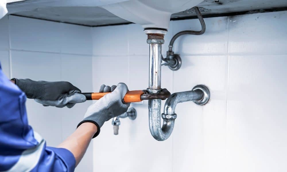 Plumber in gloves using a wrench on a bathroom sink drain pipe