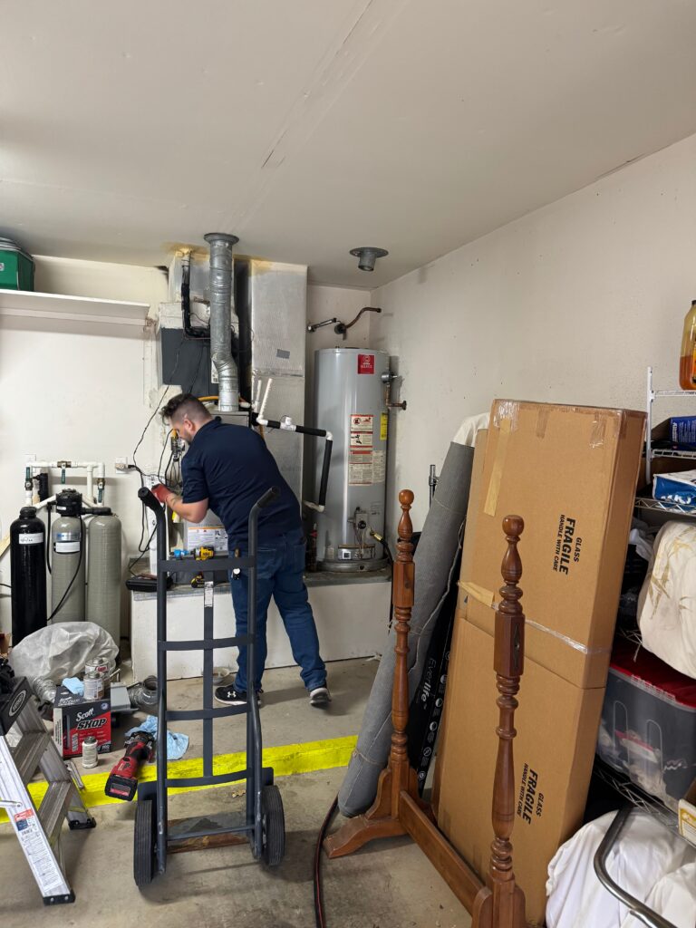 Plumber using a hand truck to move a water heater in a garage