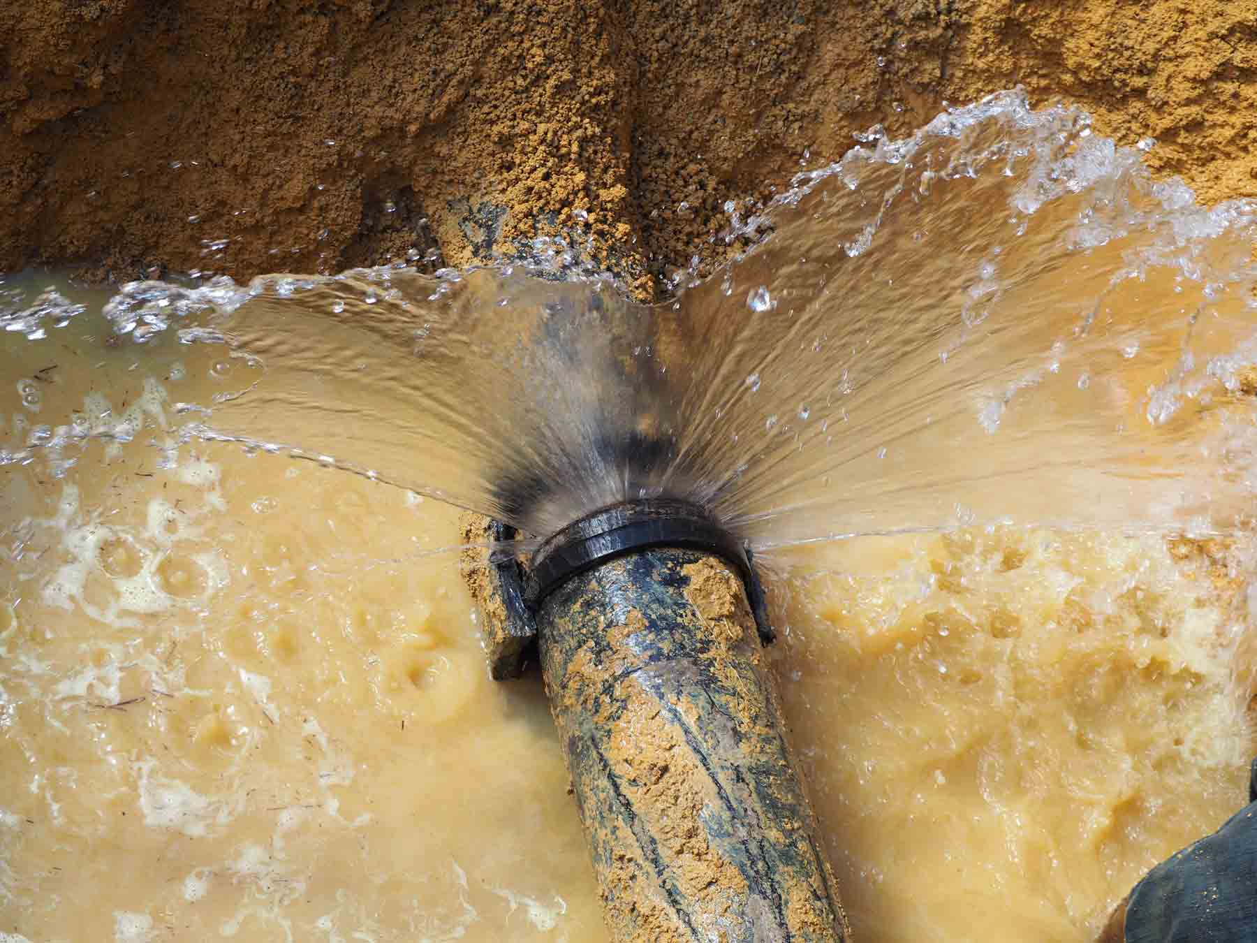Water spraying from a burst main water line joint in a muddy trench