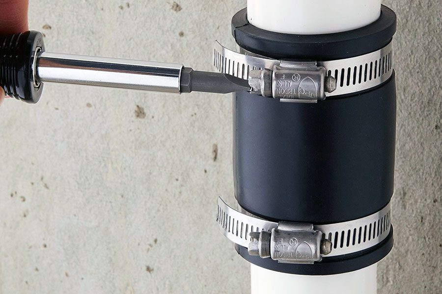 Nut driver tightening a hose clamp on a rubber pipe coupling